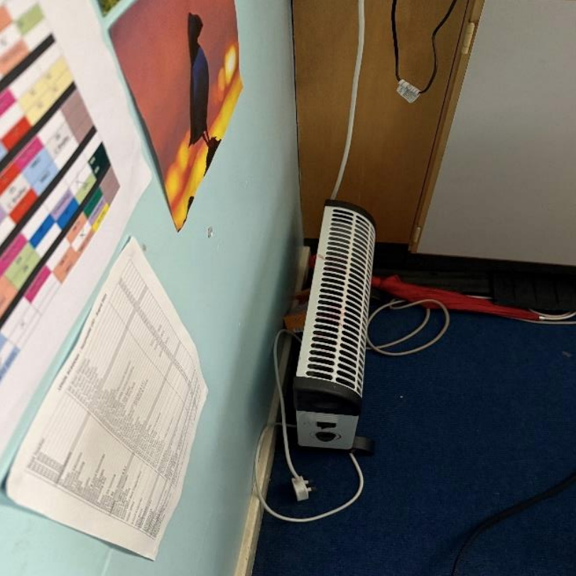A portable heater placed under a notice board covered with paperwork