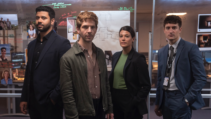 An actor in the role of Bergerac is standing slightly in front of three other actors - two male and one female. They appear to be in a police station office and they are standing in front of a clear crime scene board covered in photographs and writing.