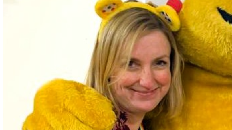 Louise wearing a floral burgundy top and yellow Pudsey head band smiling for the camera.