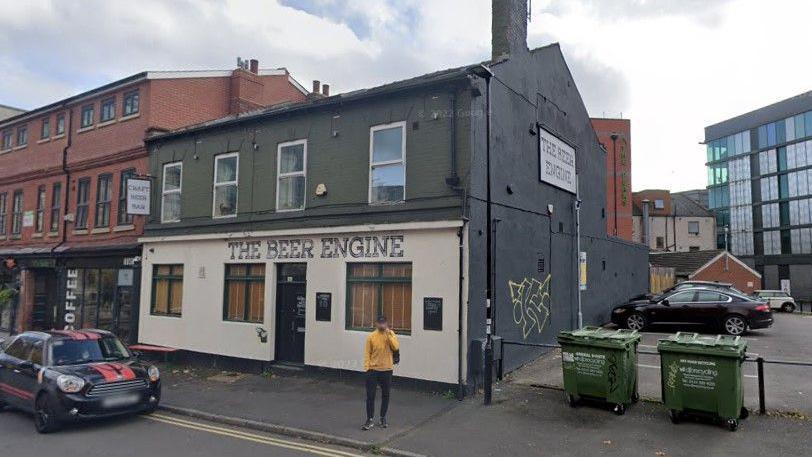 A two-storey building next to a car park with a cream front and a sign saying 'The Beer Engine'