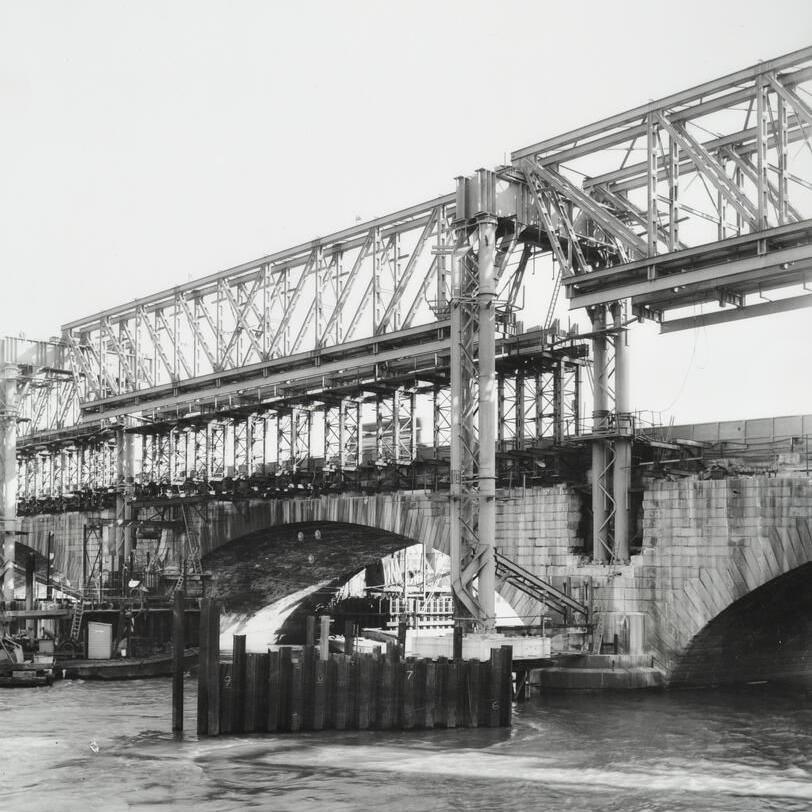 A black and white image showing the a metal frame in place of the bridge, during construction