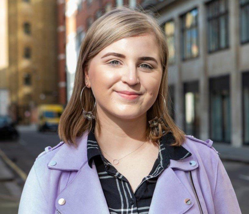 A picture of Jodie Beck wearing a lilac jacket and looking towards the camera.