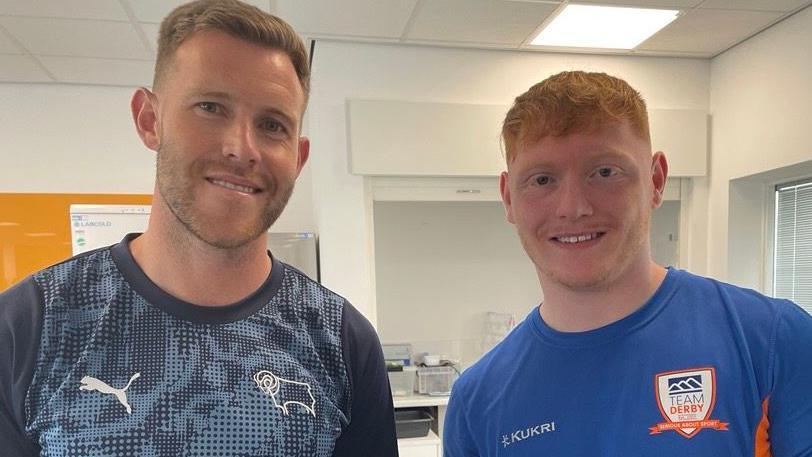 Student in blue top and ginger hair stood with Derby County defender, Callum Elder