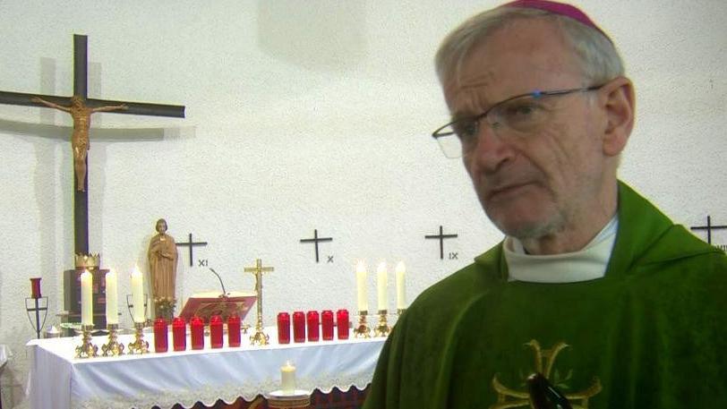 Bishop McGuckian is standing in front of an altar covered with candles. He's wearing green robes.