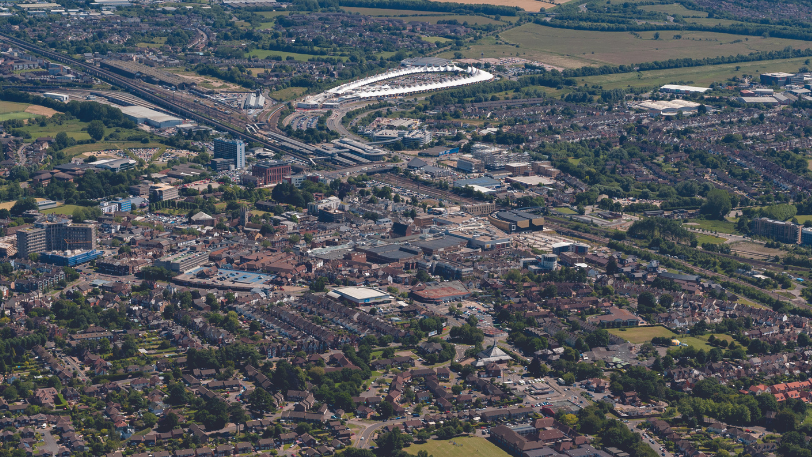 An aerial view over Ashford shows densely populated housing, green spaces and major roads