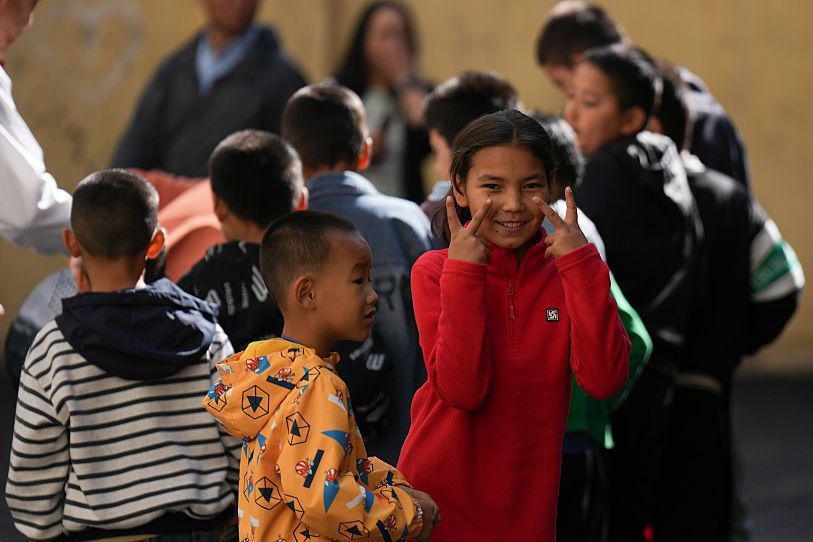 Children play on the street during an event to mark the 70th anniversary of the establishment of Xinjiang as an autonomous region of China. In the foreground are a boy in an orange, patterned jacket and a girl in a red sweater gesturing with both her hands