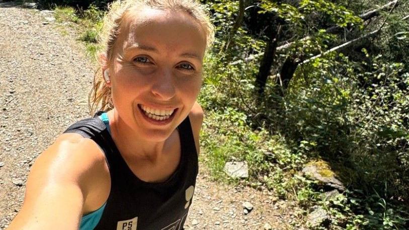 Beth Rainbow in a selfie style photo. She has blonde hair and is wearing a running singlet while on a dirt track.