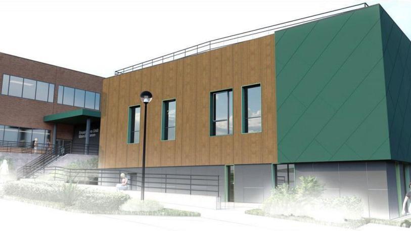 An architect's rendition of the new building, clad in brown and green with steps up to an entrance under a green canopy. 