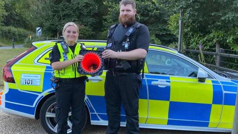 PCs Summer Bryant and Kier Dagnall, standing in front of police car,holding ducks in a traffic cone