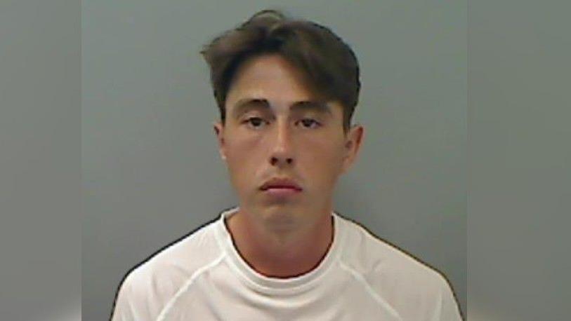 A mugshot of a man with short brown hair frowning into the camera.