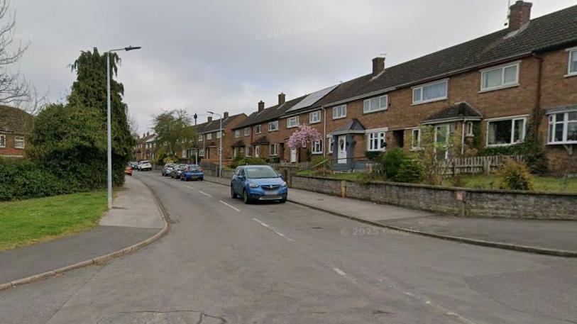 Road with houses on both sides. There are a few cars.