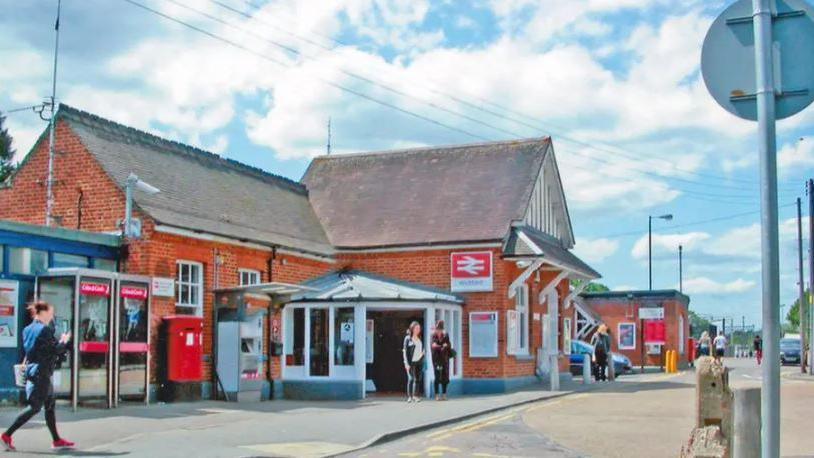 The outside of a train station. People are walking past it and in and out of the train station. 