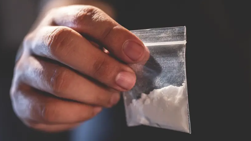 A close-up of someone's hand holding a small plastic bag containing a white powder