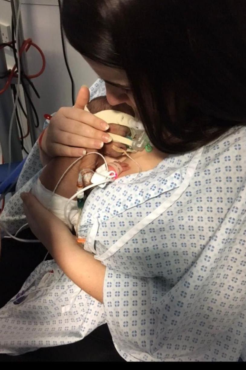 A woman with black hair cradles her son in hospital