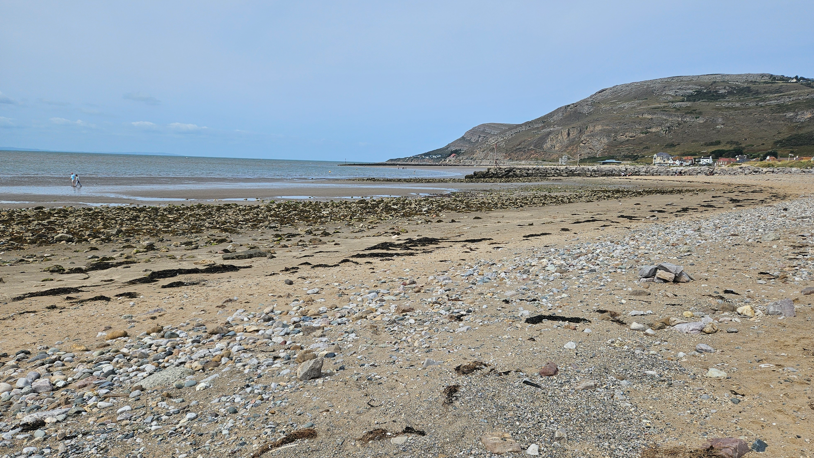 A general view of a beach with sand and stones, and the sea and cliffs behind