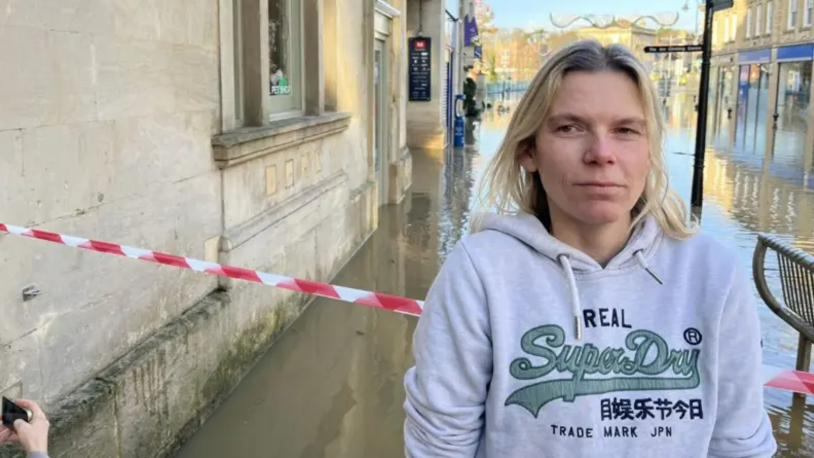 Chippenham shop owner Becky stands on Chippenham high street which is submerged under murky flood water