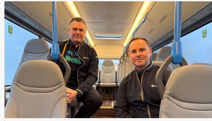 Two men sitting on the bus looking at the camera. They are sitting on different levels of seats and wearing Stagecoach branded clothes.