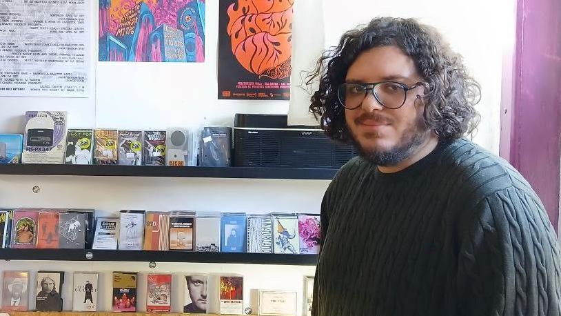 Alex Tadross stands in frong of shelves of cassette tapes