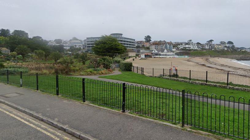 Gyllyngvase beach in the distance with grass in front of it and a stretch of road with a fence separating it.