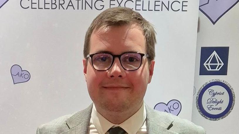 A head and shoulders image of Tom Howard, who is wearing glasses, a grey suit, white shirt and dark grey tie. He is looking straight into the camera.