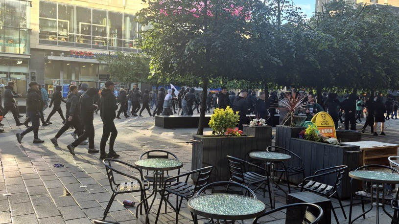 Large crowds wearing black march through Glasgow city centre. Empty tables and chairs are in the foreground