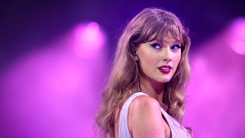 Taylor Swift smiling in front of purple lights at the Taylor Swift concert in Wembley