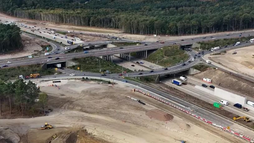 An areal view of the junction 10 improvement works being carried out on the M25 at its junction with the A3. There are dozens of vehicles driving on the road. 