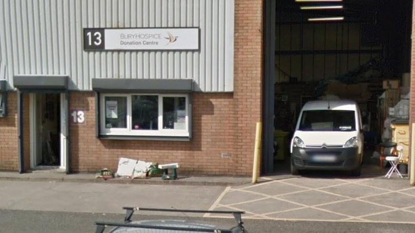 The brick and grey slats outside of Bury Hospice, with an open door and window and a white van in a loading bay