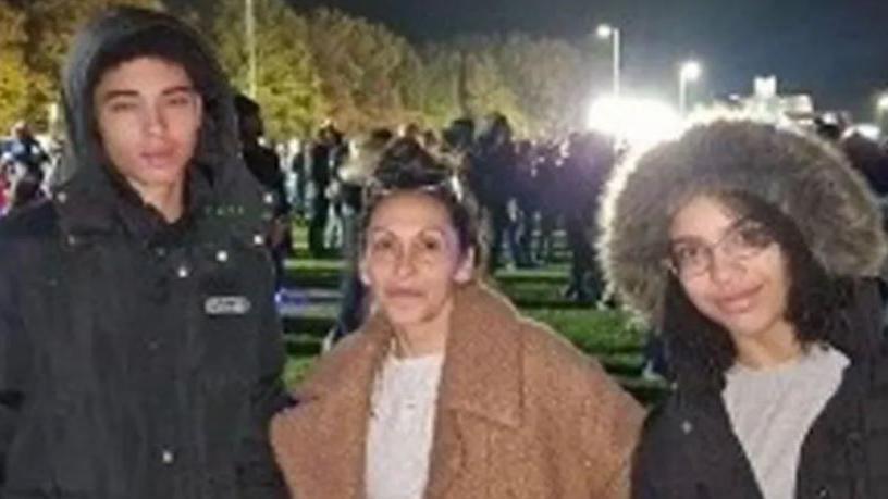 Juliana Prosper and her children smile at the camera, photographed outside in a field with a group of people behind them. 