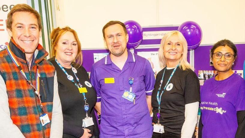 Male and female hospital staff wearing lanyards and T-shirts smiling at the camera.