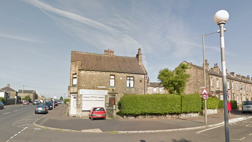 A view of an end-terrace property with the corner house converted into a shop front. There is one car parked directly outside and some on the street too.