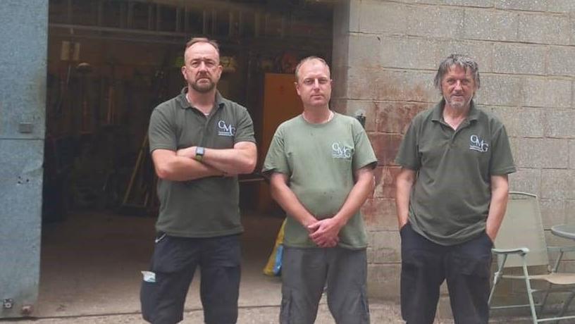 Three men standing in front of a tool shed that was broken into by thieves