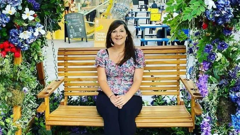 Harriet sitting on a bench swing underneath and arch made of flowers