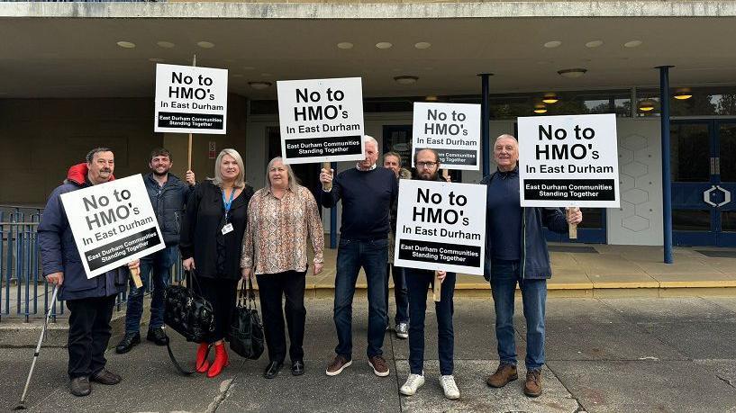 Eight people protesting outside Durham County Council's headquarters. Several of the group are holding placards reading "No to HMOs in East Durham".