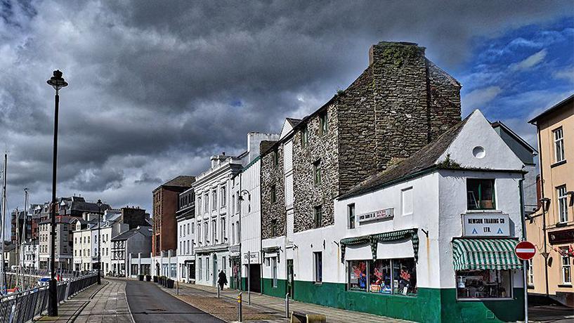 An old photo of the site, which shows the Newson's building painted white and green at the end of a terrace of buildings.