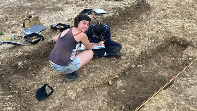 A photo showing Dr Cassie Newland from The Royal Agricultural University crouched down at the site of an archaeological dig