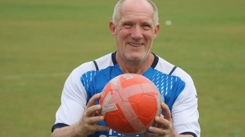 Roy wearing a blue and white jersey holding an orange football smiling for the camera 