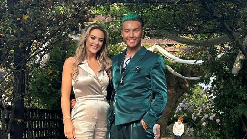 The Vivienne, James-Lee Williams (right) and their sister, Chanel Williams (left). Chanel has blonde curled hair, wears a pale pink jumpsuit and smiles at the camera, while the Vivienne wears a teal suit, has a blue stripe in their hair and smiles at the camera.