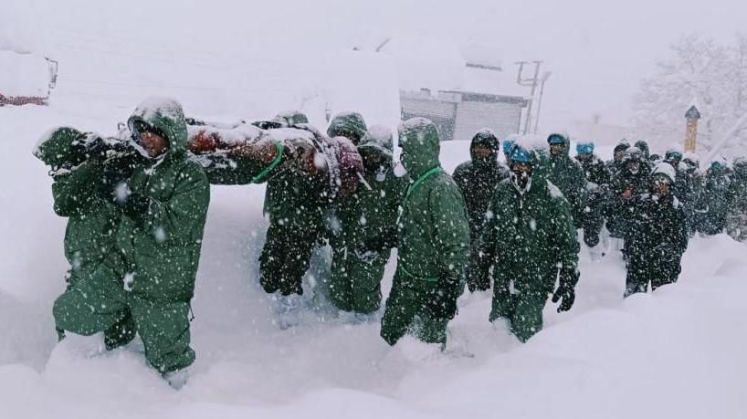 Several rescuers from the Indian Army, dressed in green overalls, trek through heavy snow after an avalanche struck a camp near Mana village in Uttarakhand state, India
