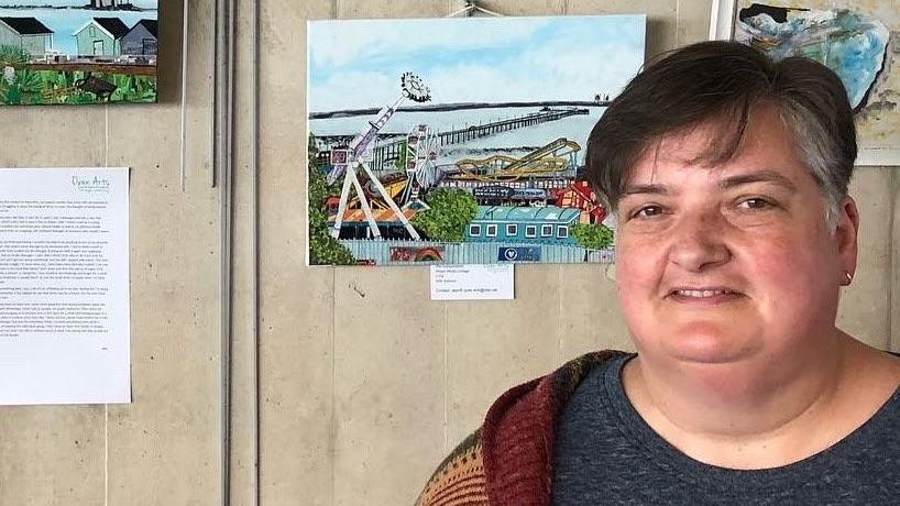 Allie Watson standing in front of artwork on the wall. The art appears to show Southend Pier and Adventure Island.