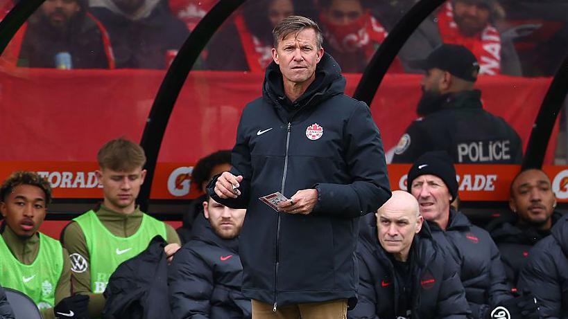 Jesse Marsch on the sidelines for Canada holding a pen and notebook 