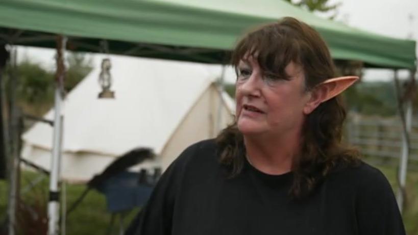 A woman dressed in a black top in a field wearing fake elf ears