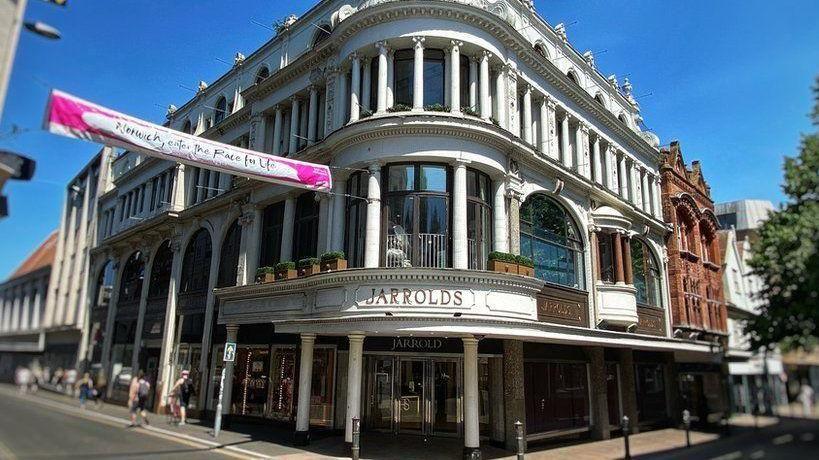 The exterior of a large department store, with its entrance on a street corner. Its frontage is white, with a gold sign reading "Jarrolds" above the door.