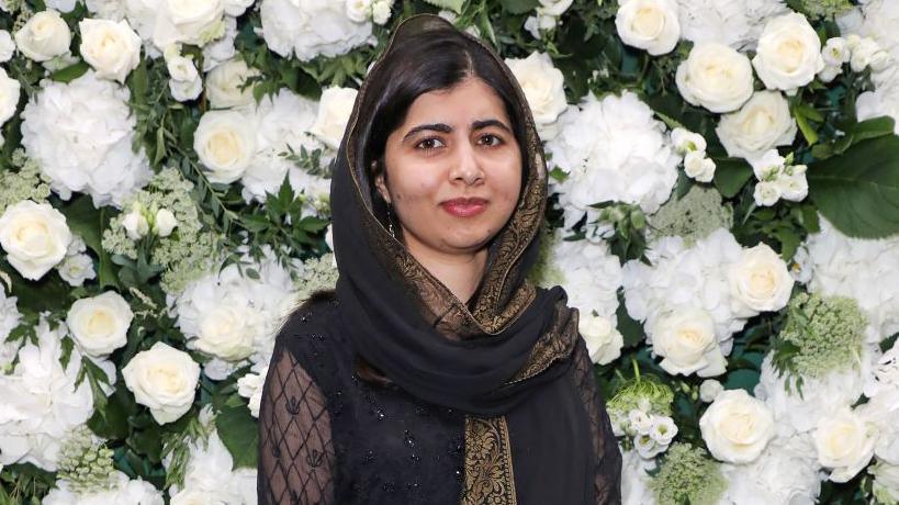 Malala standing in front of white flower background.