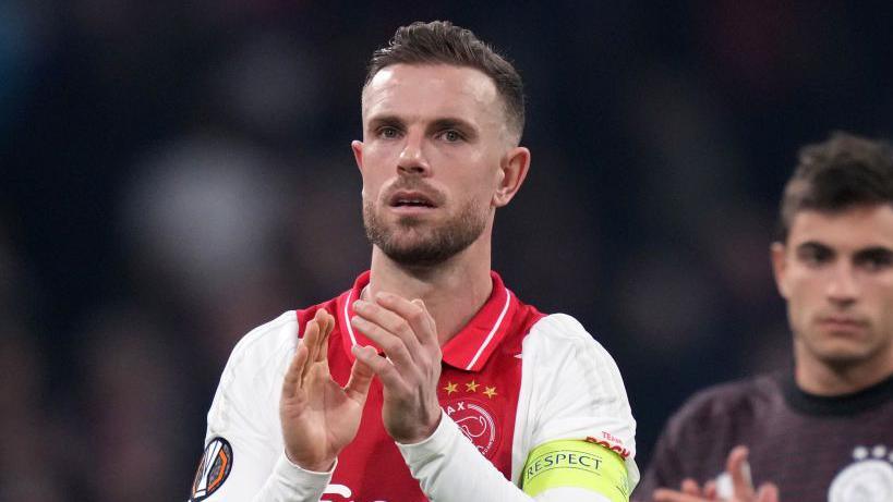 Jordan Henderson wearing a red and white Ajax shirt claps his hands