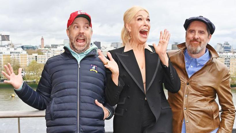 Jason Sudeikis, Hannah Waddingham and Brendan Hunt posing and smiling outside 