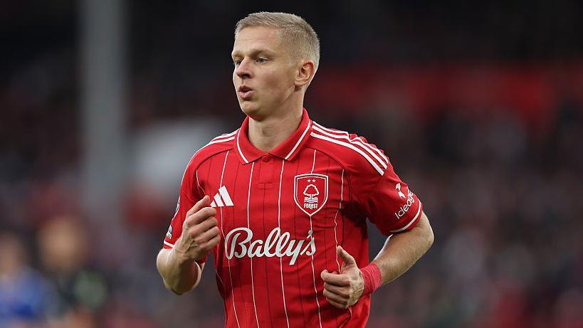 Oleksandr Zinchenko holds his arms up and is waring a red Nottingham Forest shirt