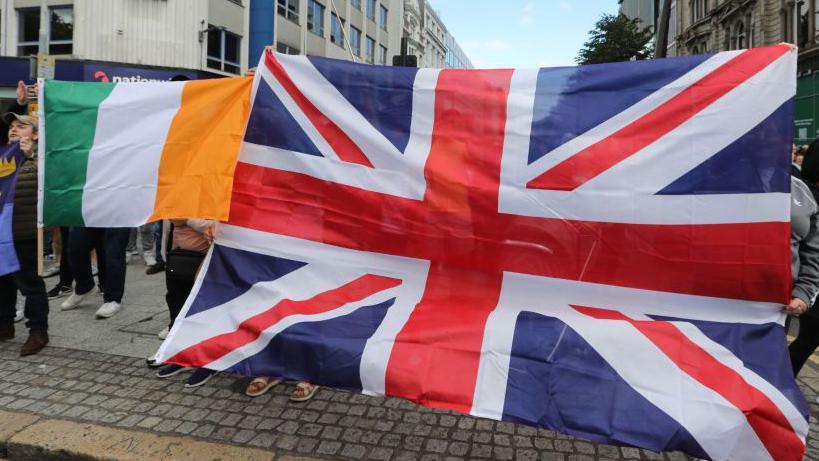 BELFAST, NORTHERN IRELAND - AUGUST 03: A Union flag and a tricolour are held up during protests in Belfast near city hall