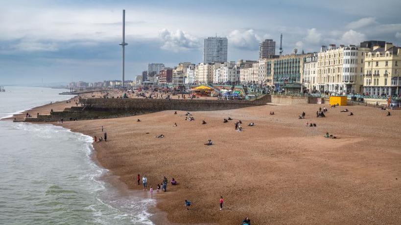 A view along the beach and seafront at Brighton taken from Brighton Pier towards the ruins of the old West Pier and the i360 tower in East Sussex, UK.