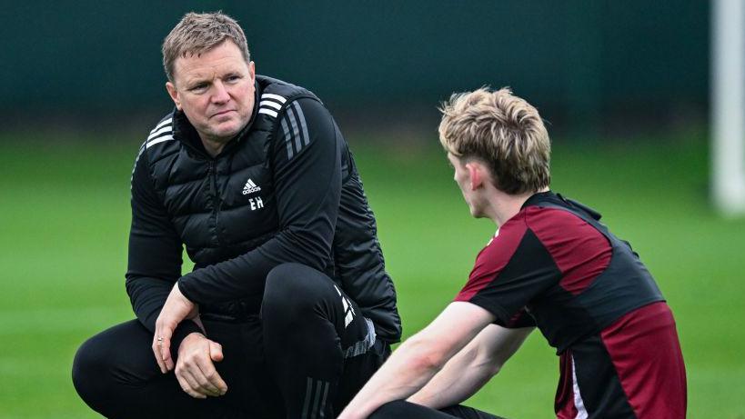 Eddie Howe and one other person talk as they kneel on a pitch